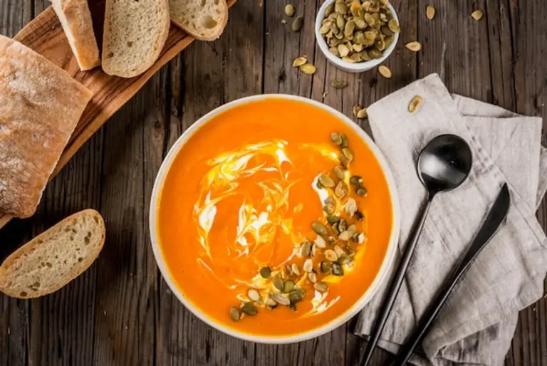 pumpkin soup top view with seeds and fresh bread autumn table