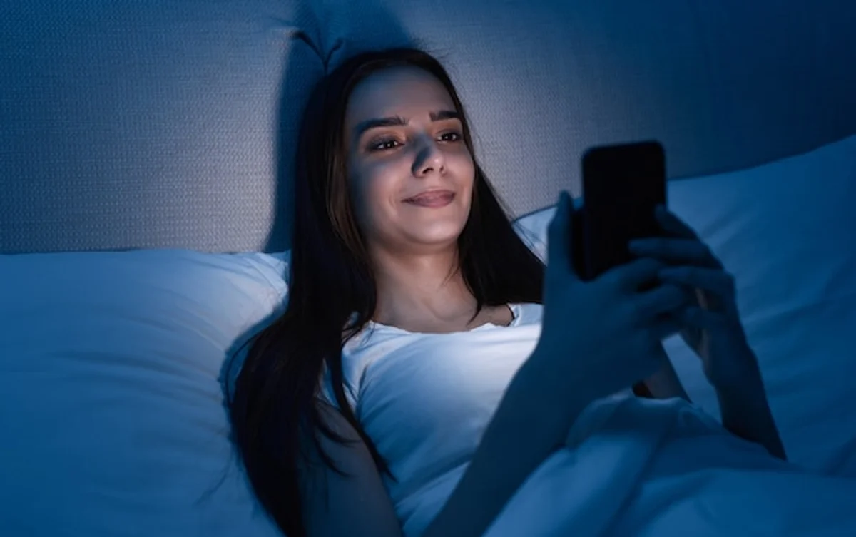 young woman using smartphone in bed night mode blue light sleep