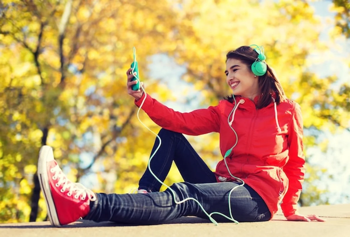 woman listening to music autumn park smiling headphones